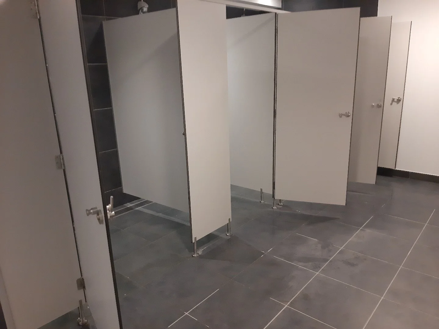 Installation de panneaux séparateurs WC en stratifié compact avec fixations inox dans des toilettes professionnelles