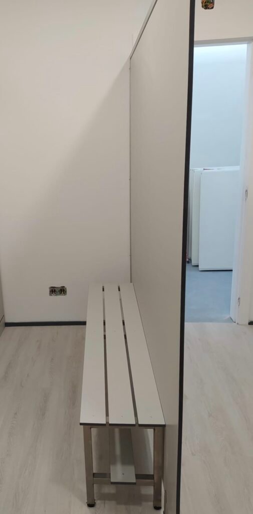 Banc vestiaire en stratifié blanc, design épuré et moderne, installé dans un espace collectif lumineux avec sol clair et murs blancs