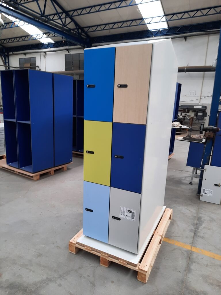 Casiers vestiaires en stratifié compact HPL avec portes multicolores (bleu, jaune-vert, beige, gris clair), équipés de serrures à code mécanique à molettes, sur palette en atelier de fabrication