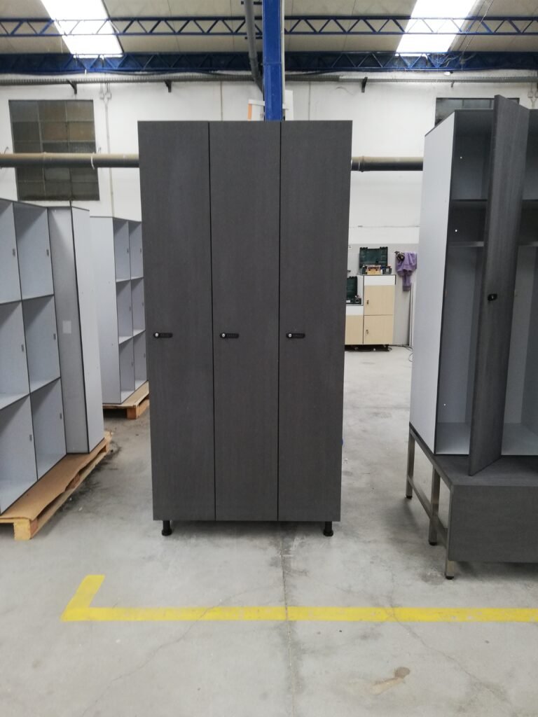 Trois colonnes de casiers vestiaires penderie pleine hauteur en stratifié compact HPL coloris gris pierre texture béton, équipés de serrures à code mécanique, photographiés en atelier de fabrication LMS