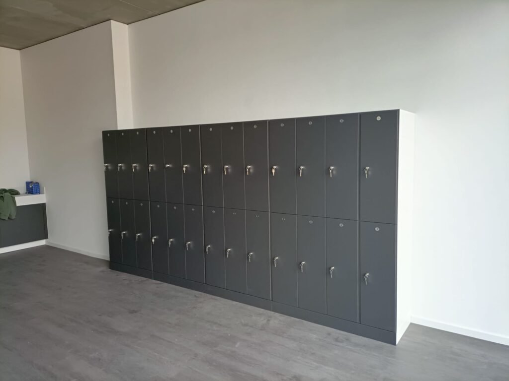 Grande batterie de casiers vestiaires en stratifié compact HPL coloris anthracite, configuration 3 cases par colonne, équipés de serrures à clé, installés dans un vestiaire d'entreprise aux murs blancs